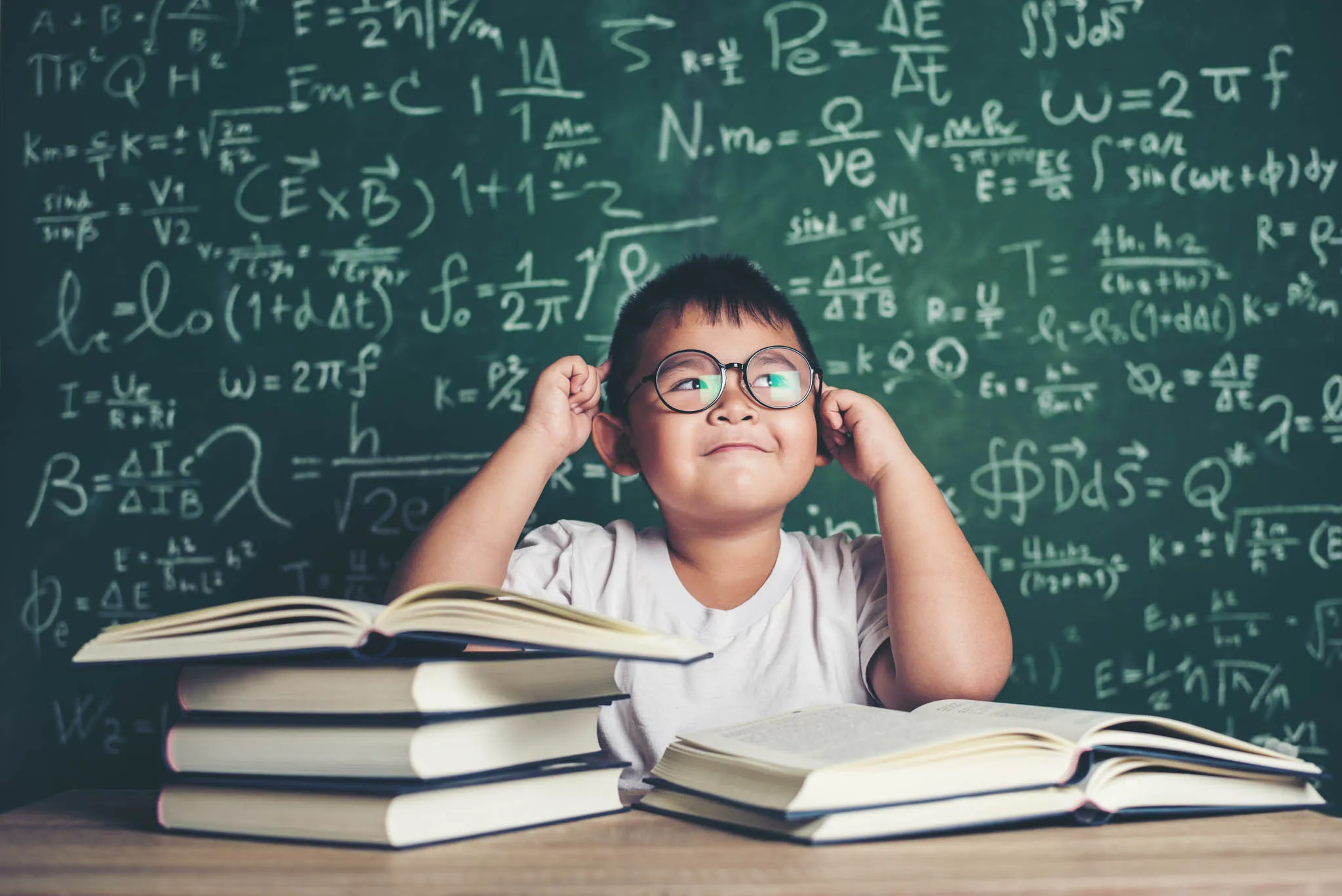 Niño con libros frente a una pizarra, representando lectura, análisis y pensamiento crítico.